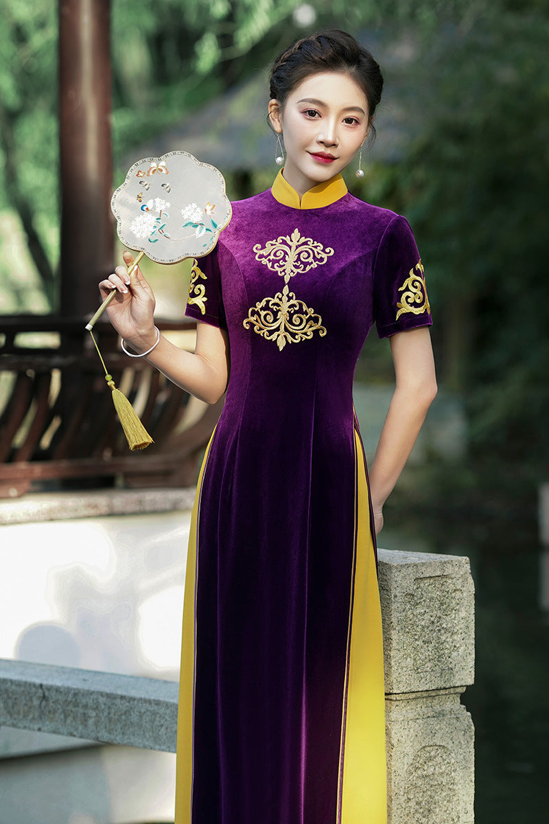 Front-facing view of the Imperial Plum Traditional Ao Dai Dress, featuring luxurious purple velvet fabric with ornate gold embroidery on the chest and sleeves. The modern Vietnamese ao dai design is complemented by golden side panels and a high mandarin collar, photographed outdoors with soft natural lighting for a royal-inspired look.