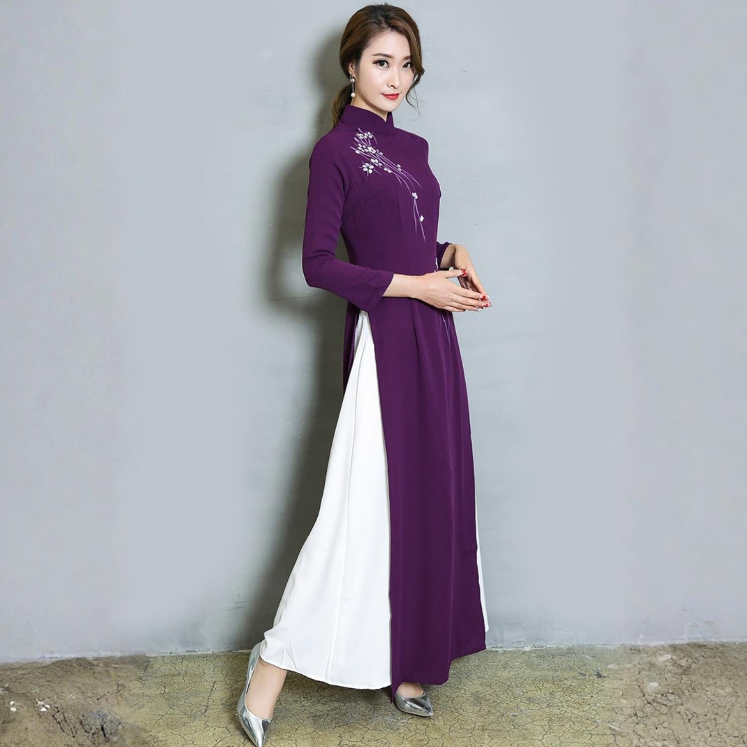 Three-quarter angle full-length shot of a woman wearing a purple modern Vietnamese Ao Dai dress with white side panels, photographed under studio lighting.