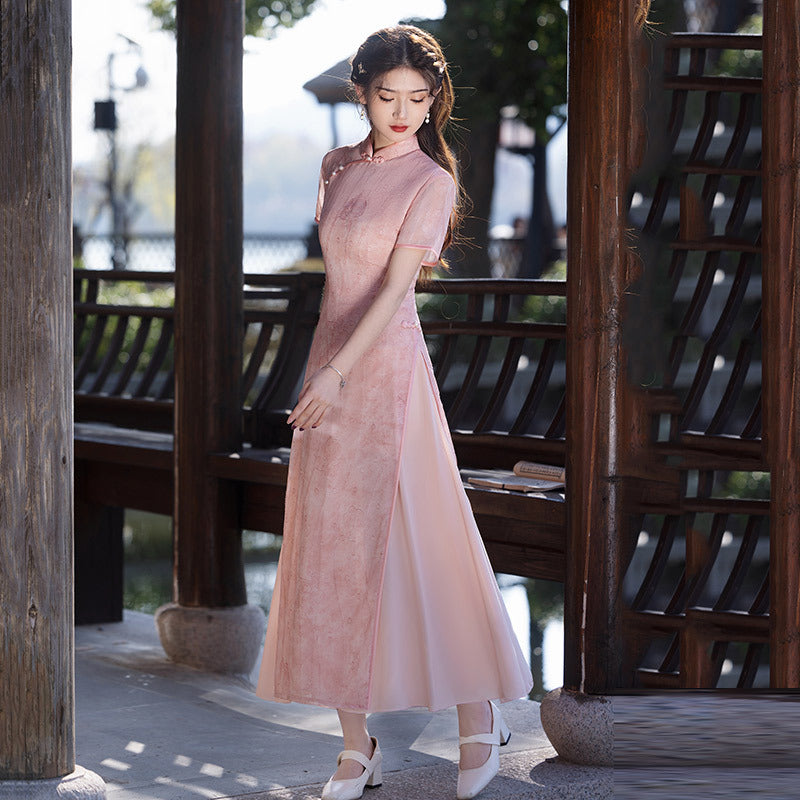Side profile standing shot of the Silken Lake Modern Ao Dai Dress in pink, showing the long A-line skirt and gentle drape; woman posed beneath wooden pavilion beams; modern ao dai elegance in soft afternoon light.