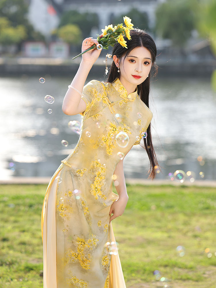 Close-up dynamic pose of a woman in an embroidered traditional modern ao dai, surrounded by floating bubbles in warm outdoor lighting