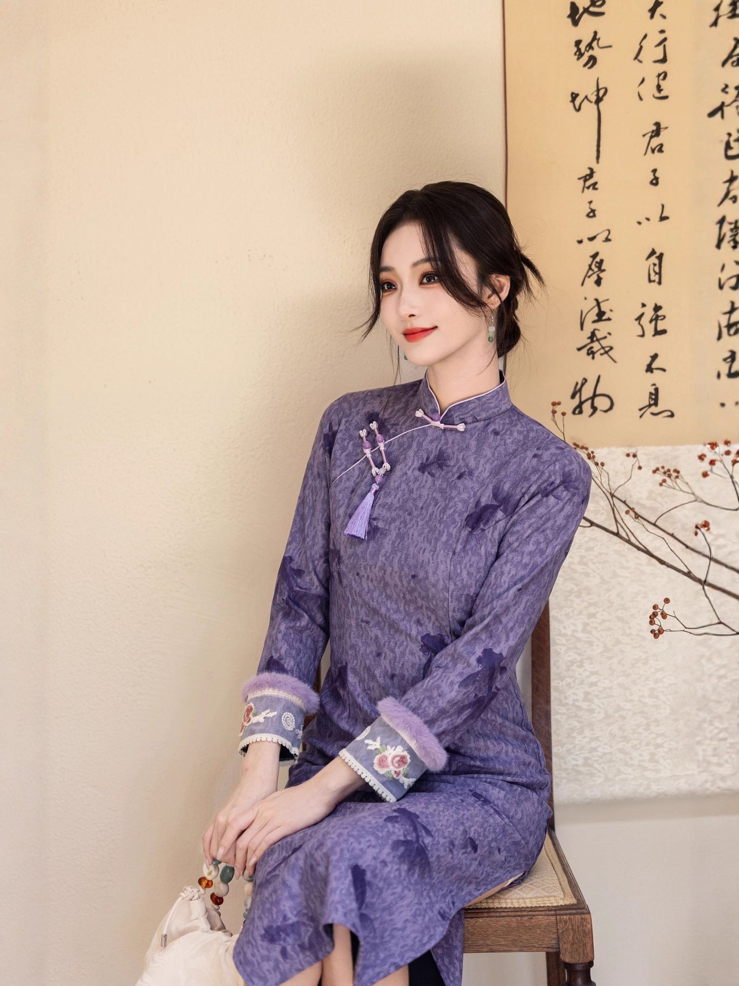 Close-up seated view of the model wearing the Twilight Silk Modern Ao Dai Dress, showing the delicate embroidered cuffs and matching tassel detail near the collar. The look emphasizes its refined craftsmanship and timeless femininity.