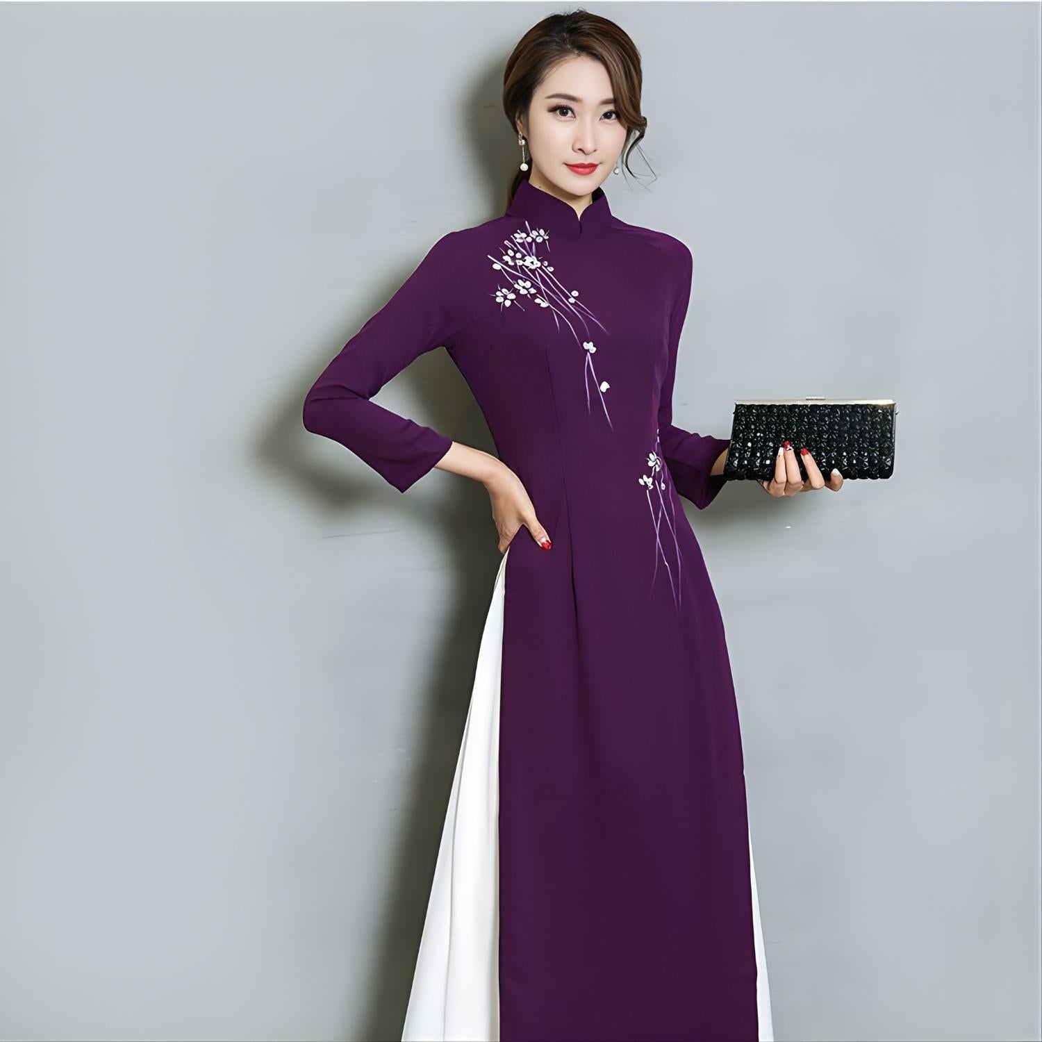 Front view of a woman wearing a purple Vietnamese Ao Dai dress with floral embroidery and white side panels, taken under studio lighting.